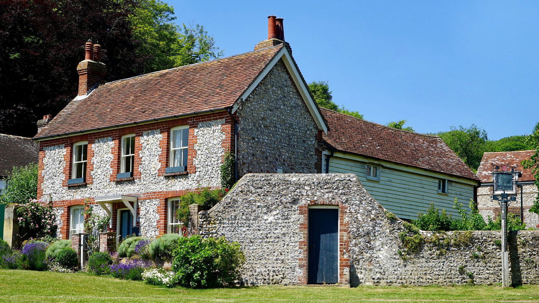 A traditional country house with flint walls, red brick details and a flowering garden.